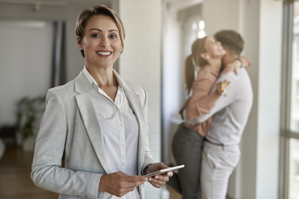 Portrait of happy real estate agent with joyful couple in the background